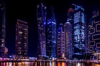 Illuminated skyscrapers of Dubai Marina at night, reflecting on the water.